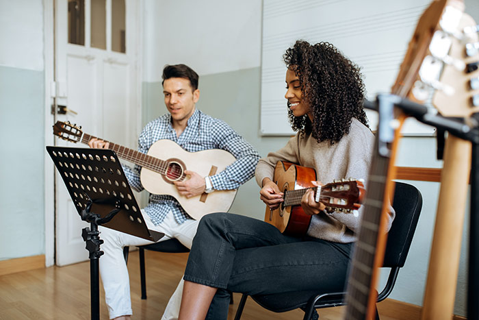 Man and woman playing guitars by looking to paper