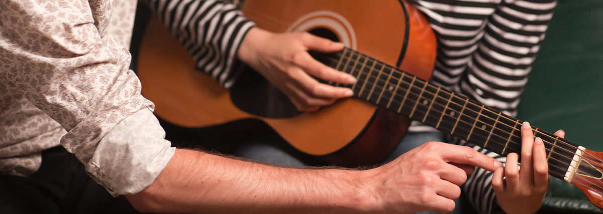 Man hand fixing hand position of woman with guitar playing