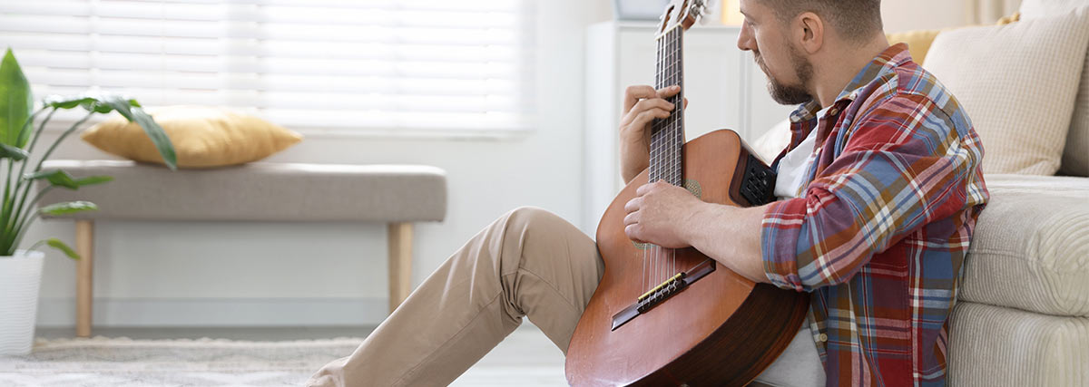 Man sits in front of sofa by playing guitar