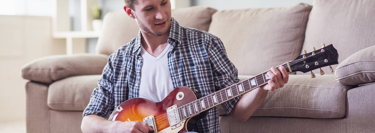 Man with electric guitar sitting in front of the couch