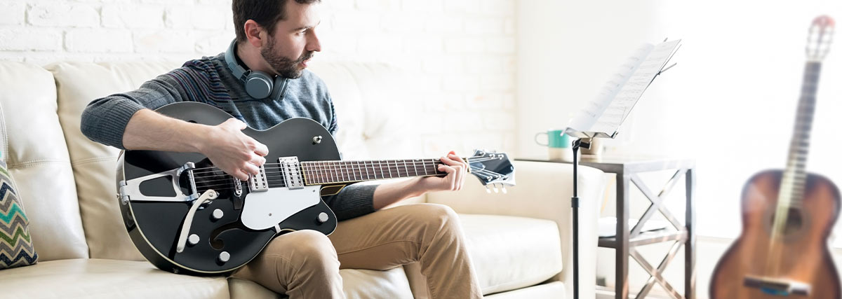 Man with headphone playing guitar by looking to music papers