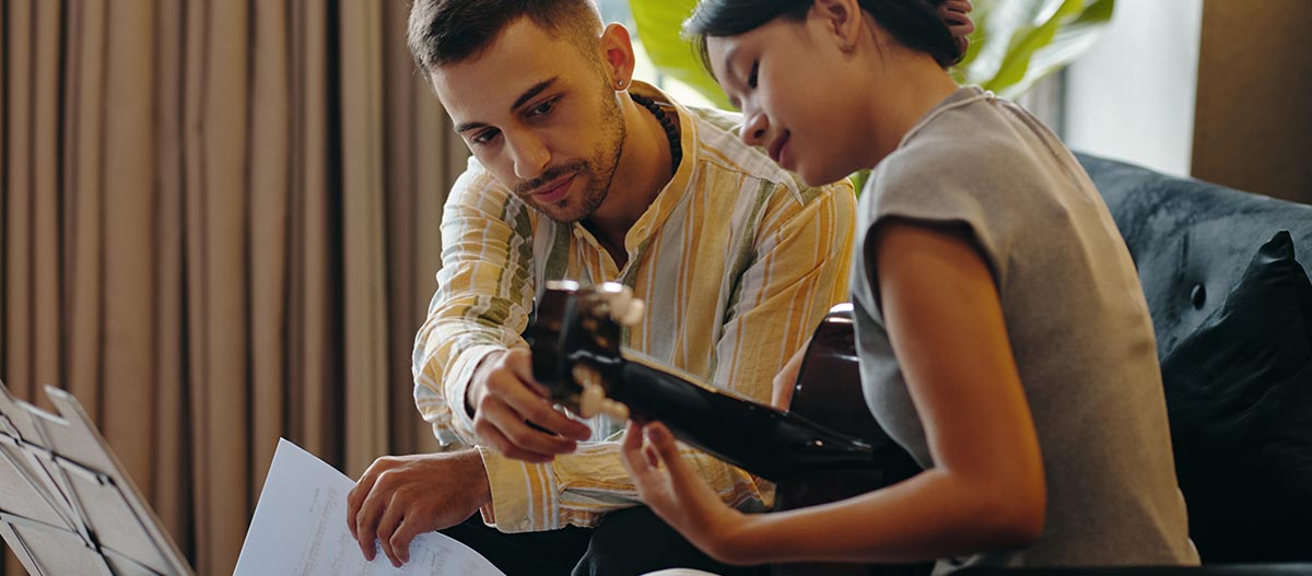 Guitar teacher helping a young student read sheet music during an acoustic guitar lesson
