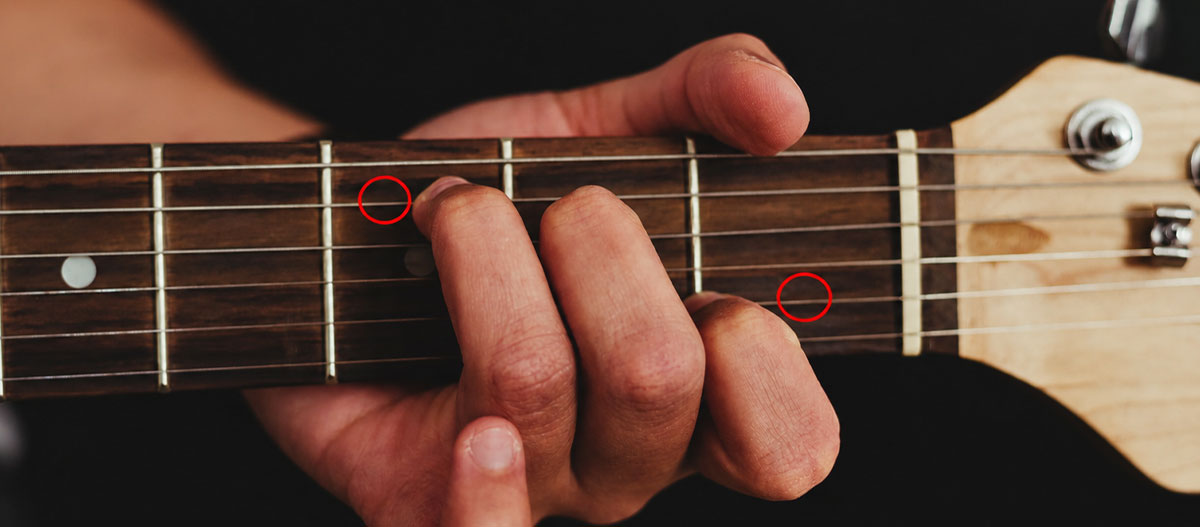 Close up of guitar fretboard showing correct octave shape finger position