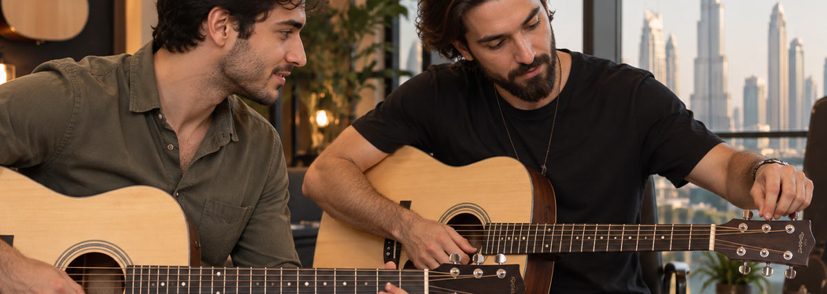 Adult guitarists learning how to tune acoustic guitars during a guitar lesson in Dubai